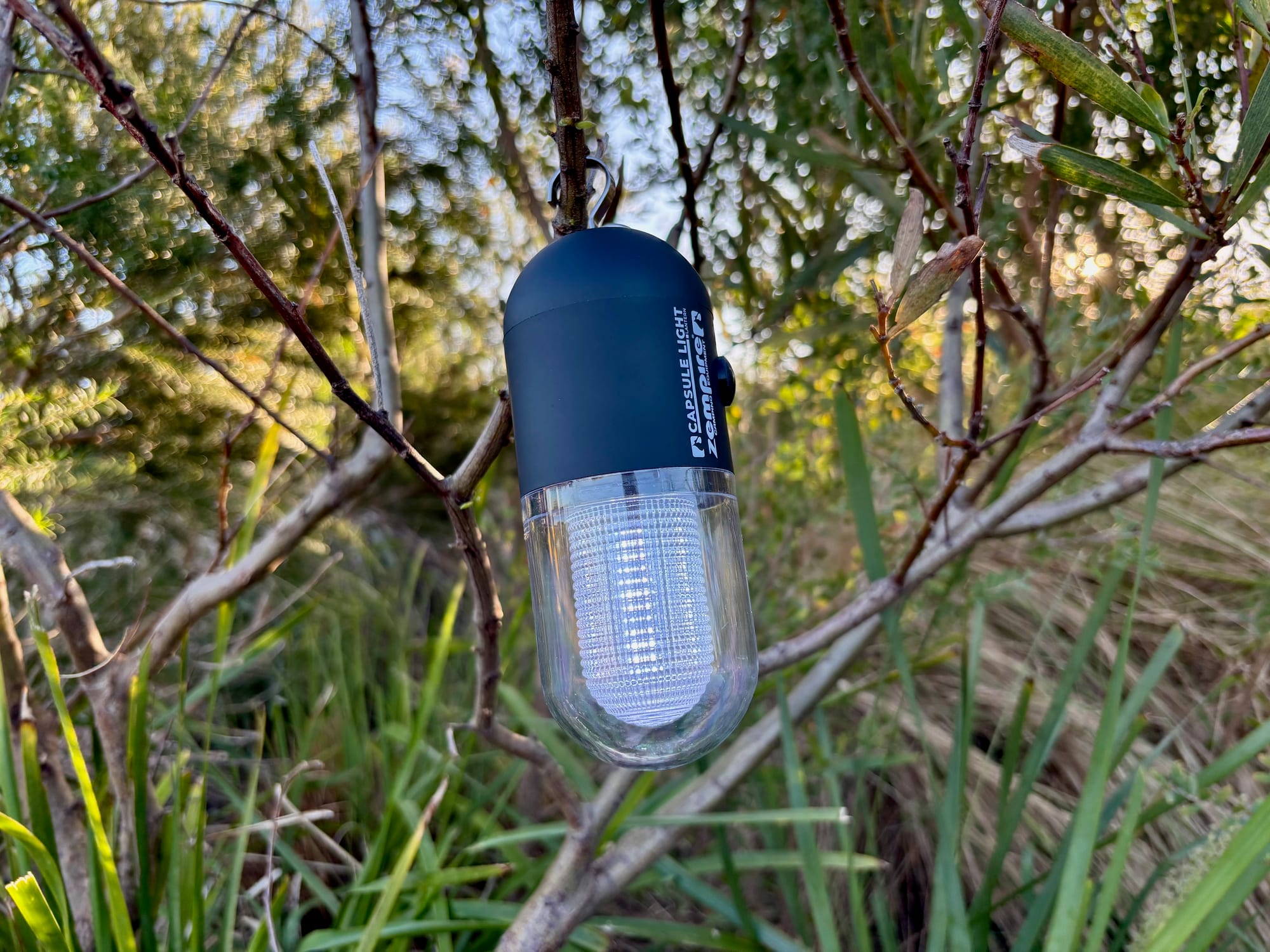 The Zempire Capsule Light switched on, hanging from a branch