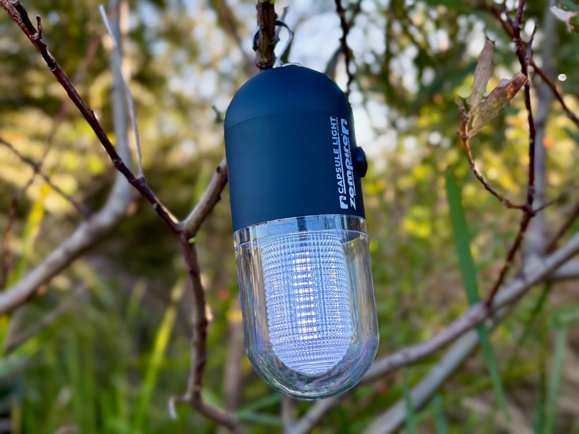 The metal hook of the Zempire Capsule Light hooked over a thin branch