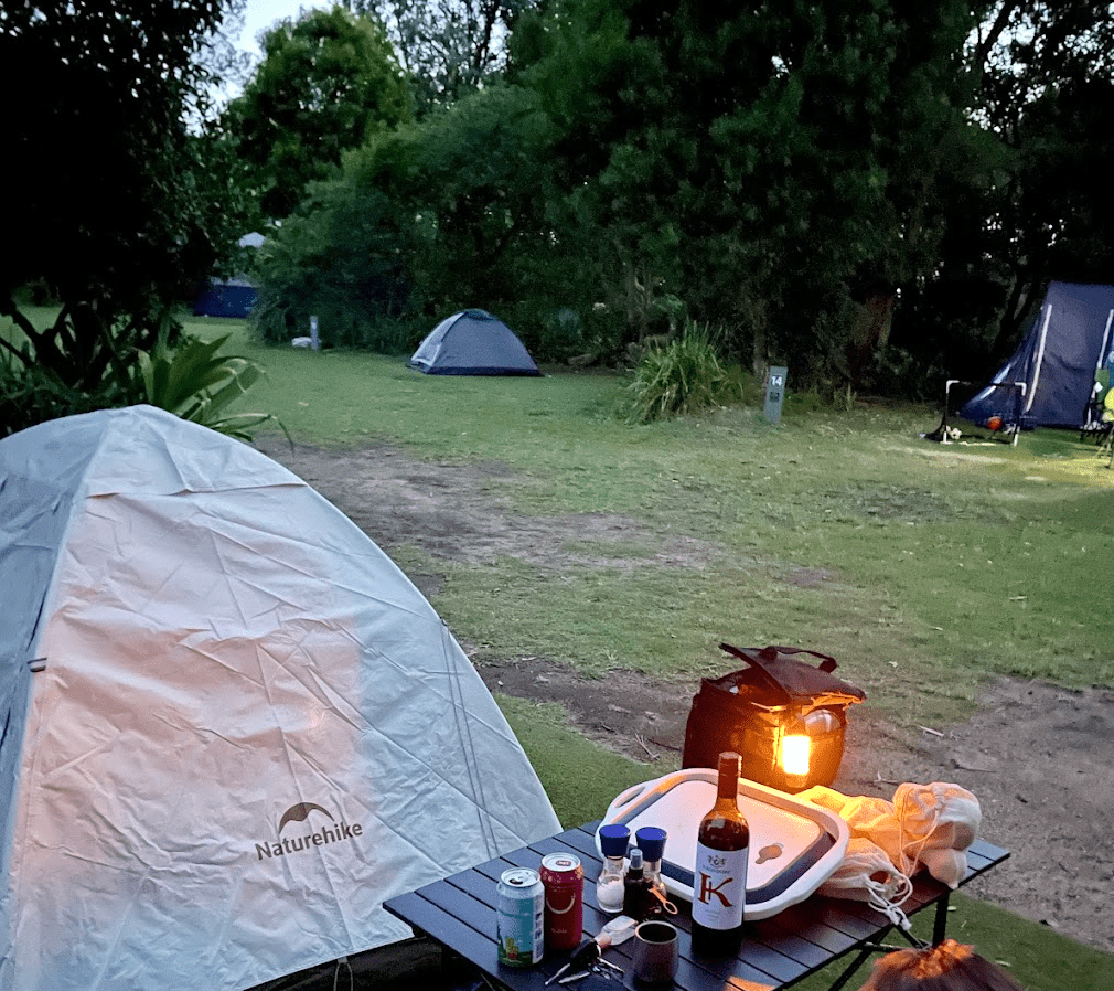 A tent and a camp table with a lantern on the grass at Putty Beach Campground