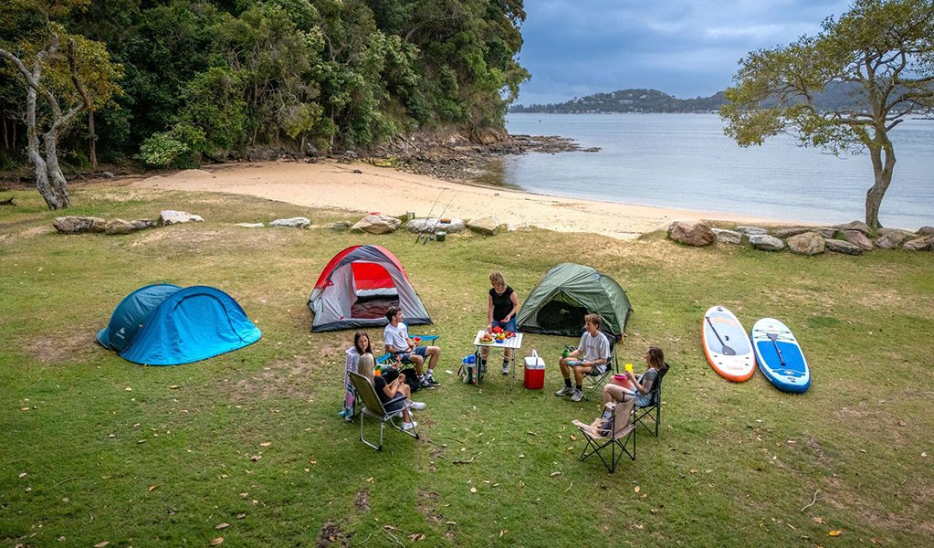 Tents, kayaks and campers on the grass by the beach at The Basin Campground