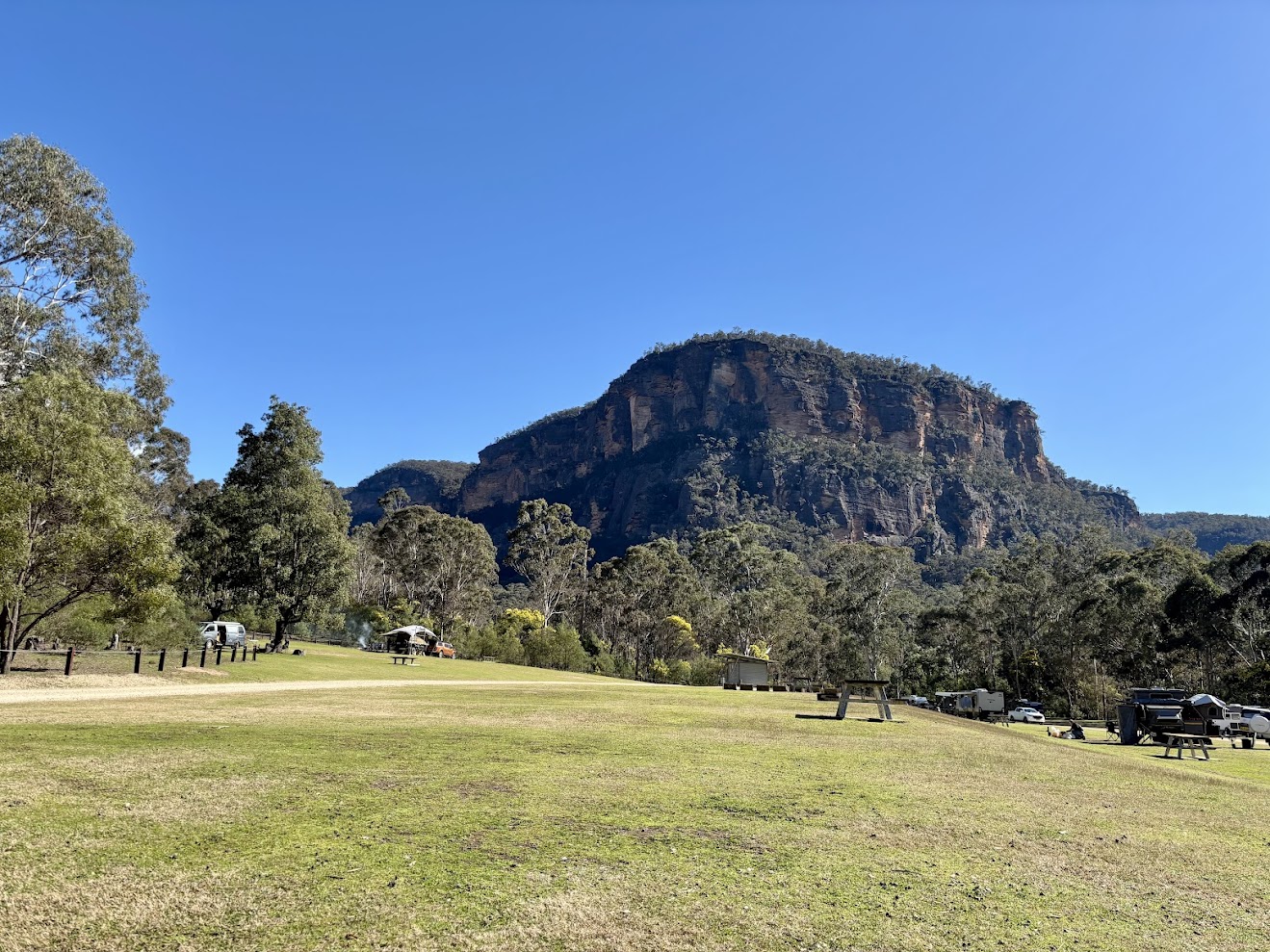 The open grass camping area at Coorongooba Campground with the cliffs above