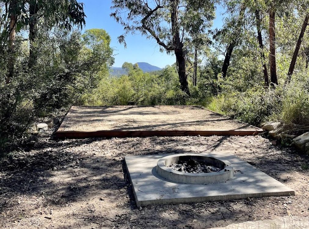 A fire pit and gravel tent pad at Finchley Campground, looking towards Mount Yengo