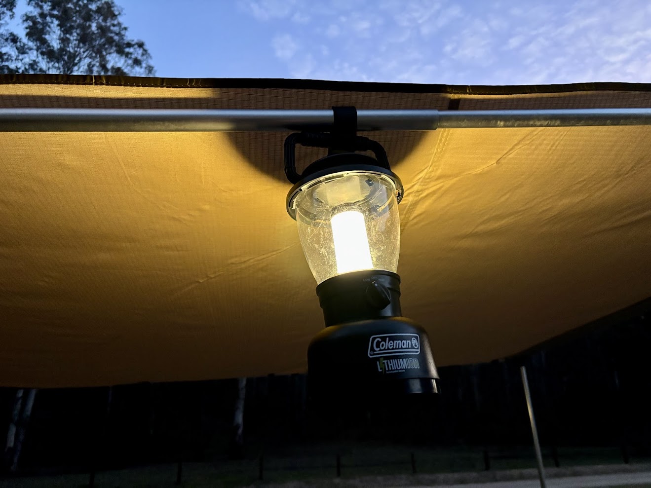 The Coleman lantern hanging under the awning at Coorongooba Campground, lit up